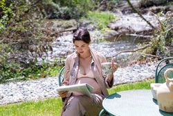 Pregnant young woman reading newspaper outside