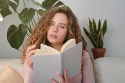 female reading book and looking at camer