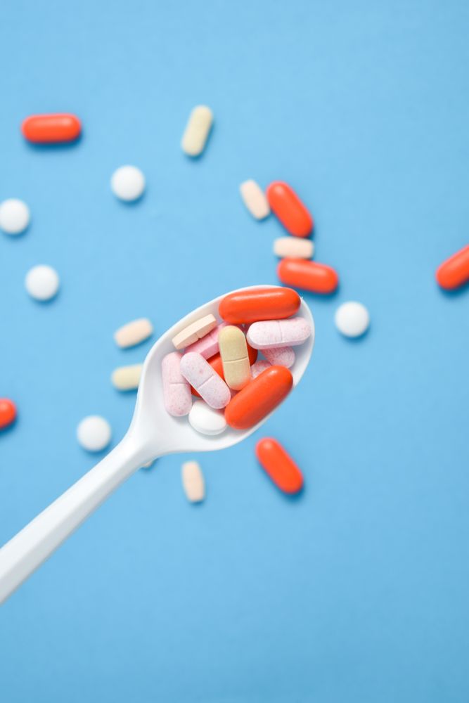 Plastic spoon with various colorful pills over blue table with copy space