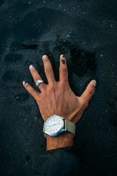 Person putting hand with watch on dark sand