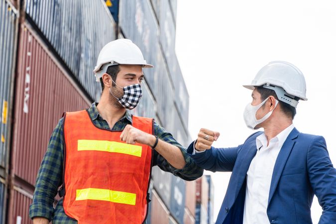 Construction site worker and foreman wearing hygiene face mask elbow bump greeting