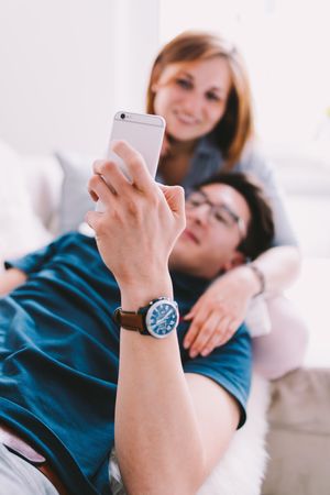Couple relaxing with man leaning back on woman looking at smartphone