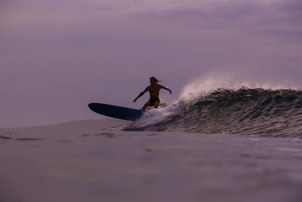 Man on surf board on waving water at sunset