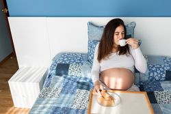 Tender pregnant woman having breakfast on bed