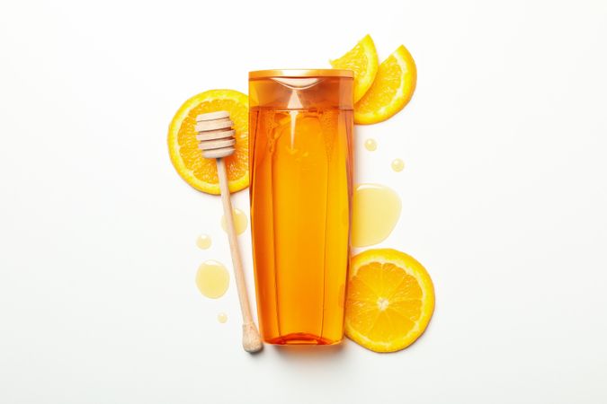 Shampoo bottle, orange slices and dipper on light background. Natural cosmetics