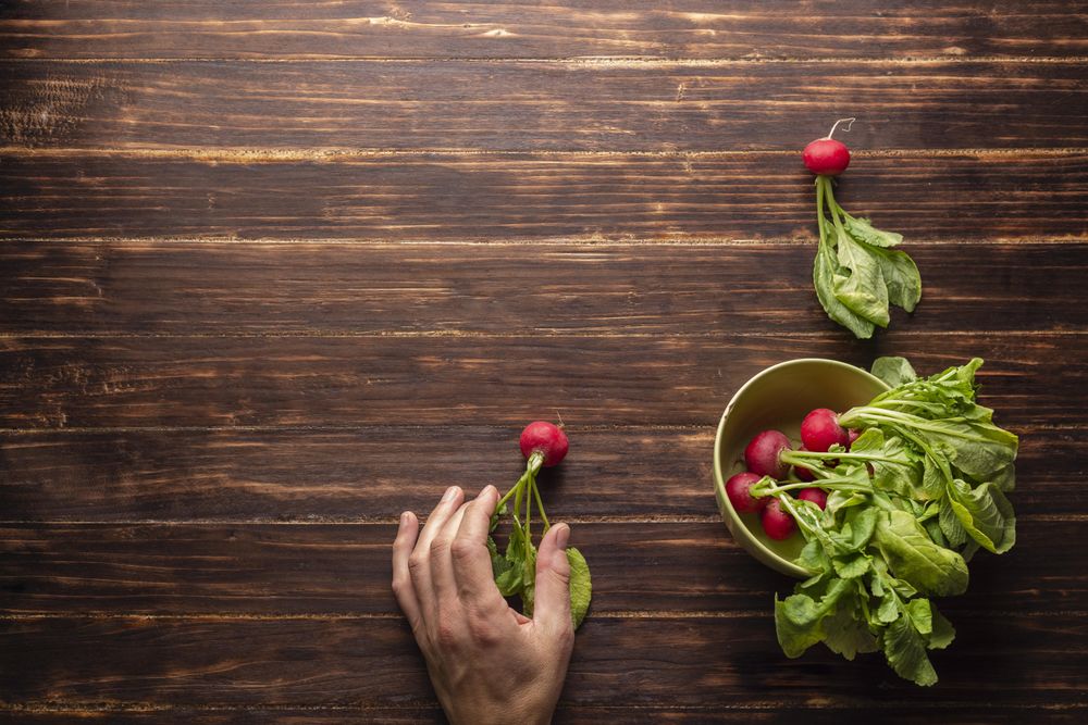 Person holding radish beside a bowl of radishes