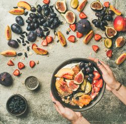 Woman with yogurt bowl over fruit assortment with figs, grapes, peaches, and chia seeds, square crop