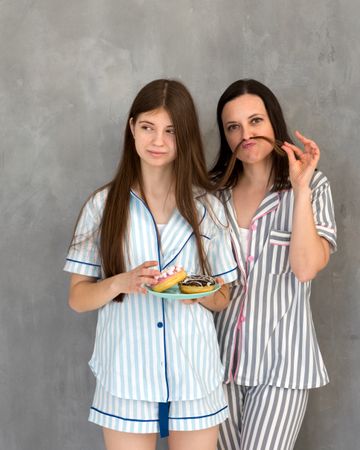 Two people in pajamas making moustaches with hair, laughing.