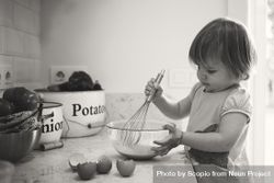 Grayscale photo of toddler mixing eggs in kitchen bG6dv4