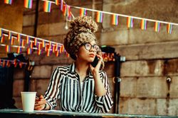 Black woman in stripe shirt taking phone call in cafe