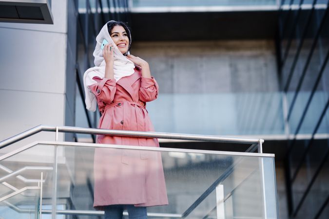 Female in headscarf and pink trench coat standing on staircase with phone, copy space