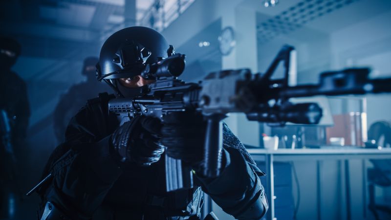 Close Up Portrait of Masked Squad Member of Armed SWAT Police Officers Who Storm a Dark Seized Office Building with Desks and Computers