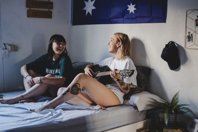 Lesbian couple playing guitar on bed