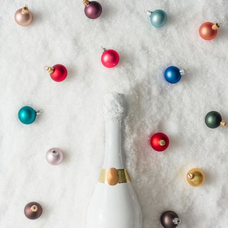 Champagne bottle in snow with colorful Christmas baubles