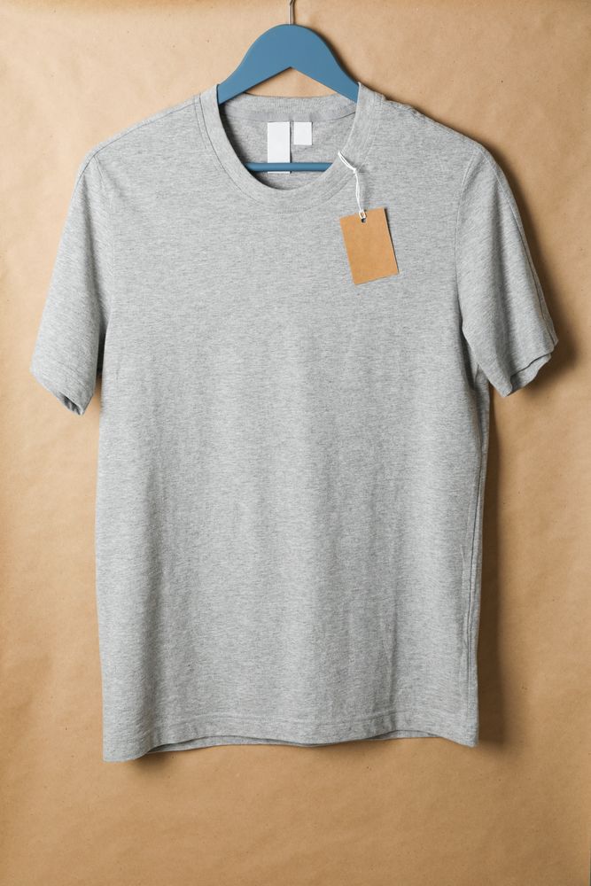 Hanger with blank gray t-shirt and tag on cardboard background, space for text
