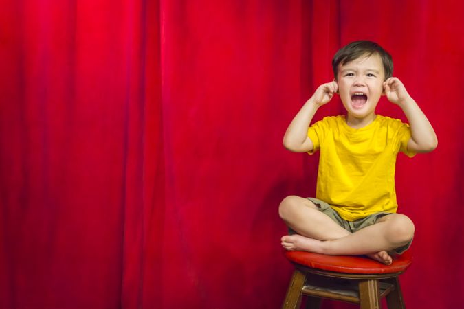Boy, Fingers In Ears on Stool in Front of Curtain