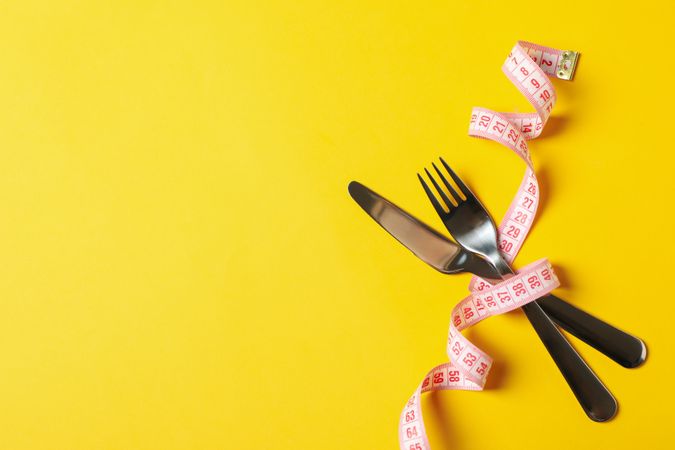 Cutlery with measuring tape on yellow background