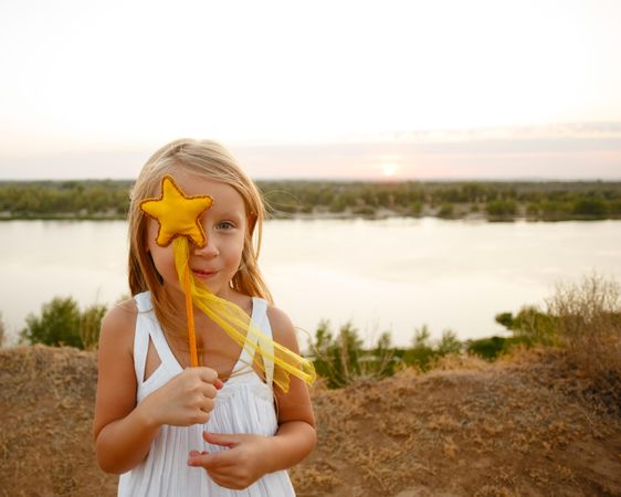 Blonde female child in dress holding up star wand in front of face