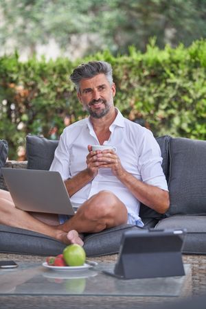 Mature businessman with netbook drinking coffee outside