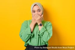 Shocked Muslim woman in headscarf and green blouse with both hands over her mouth 4jeo85