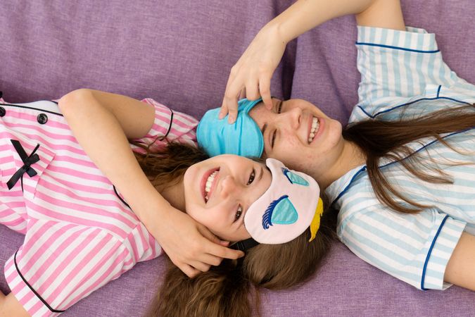 Sisters lying on couch laughing with eye masks on.
