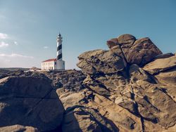 Lighthouse located on rocky coast in countryside under cloudless