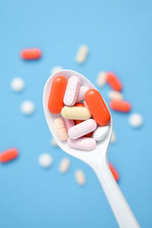 Plastic spoon with various colorful pills over blue table
