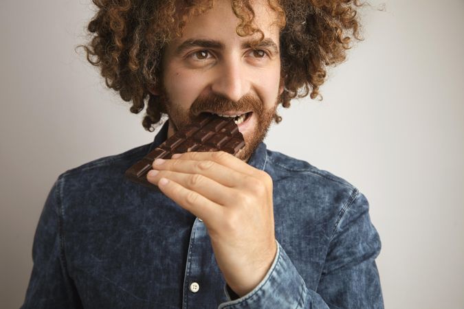 Man with curly hair eating chocolate bar