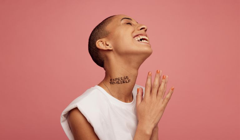 Female with shaved head smiling on pink background
