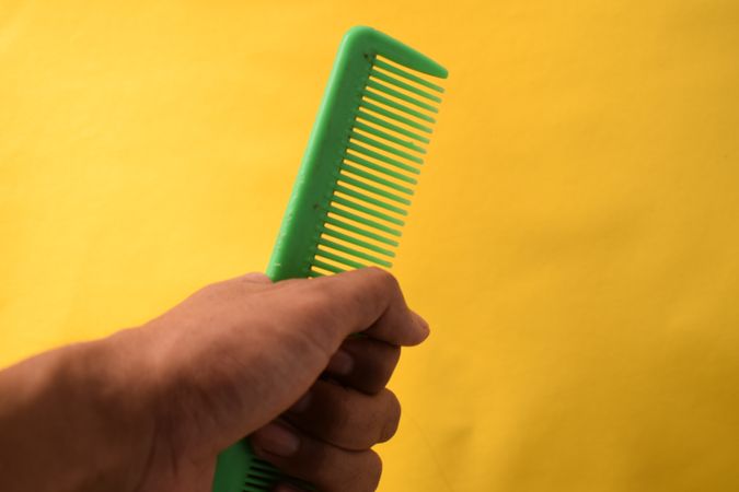 Hand with green hair comb against yellow background