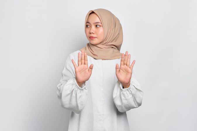 Serious Asian female in headscarf with both hands up