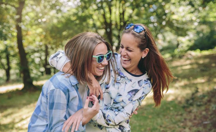 Happy women embracing and laughing over nature background