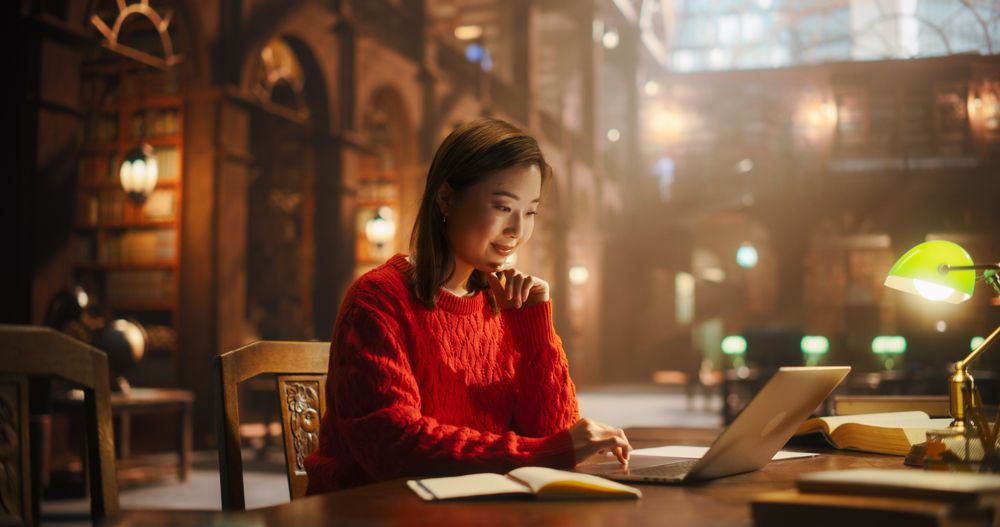 Thoughtful Multiethnic Asian College Student Using Laptop Computer to Study in a Classic Library