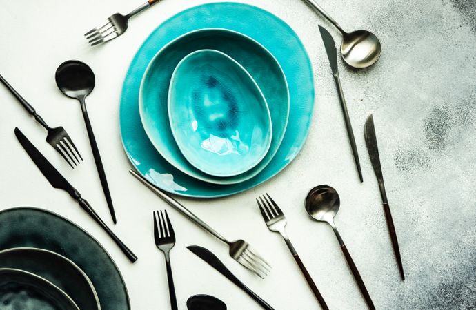 Top view of full teal table setting surrounded with silverware with on grey background