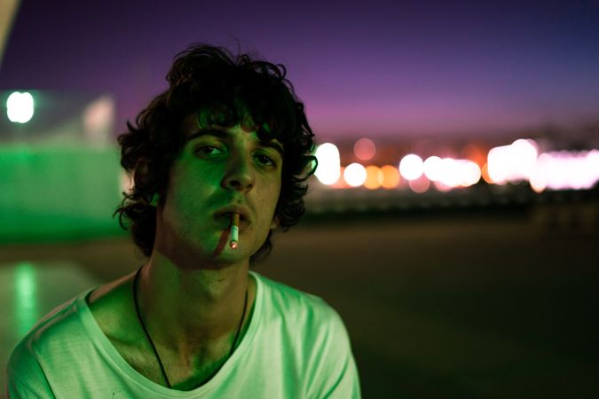 Adult man smoking while looking at camera during sunset