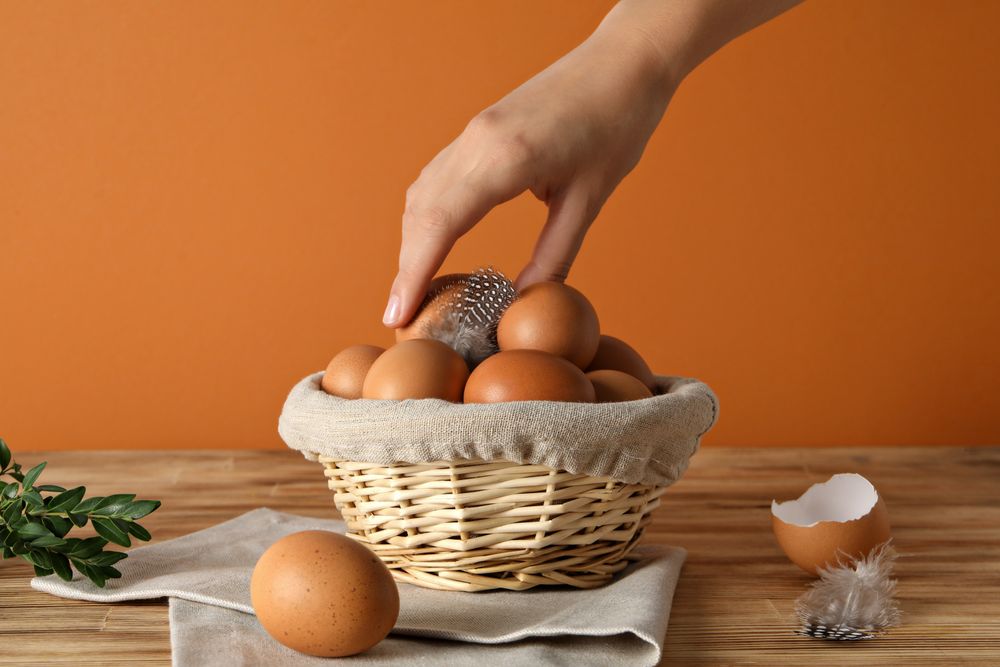 Eggs in a wicker basket, with a hand, on an orange background.