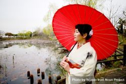 Woman in light kimono holding red umbrella standing on dock 0yQpG0
