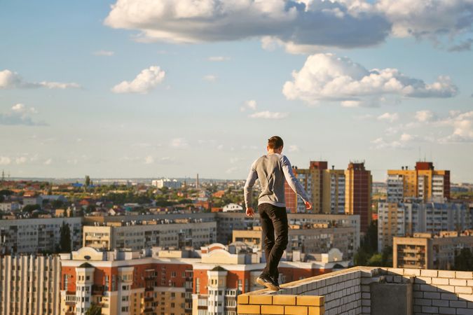 Back of male balancing on wall high above city