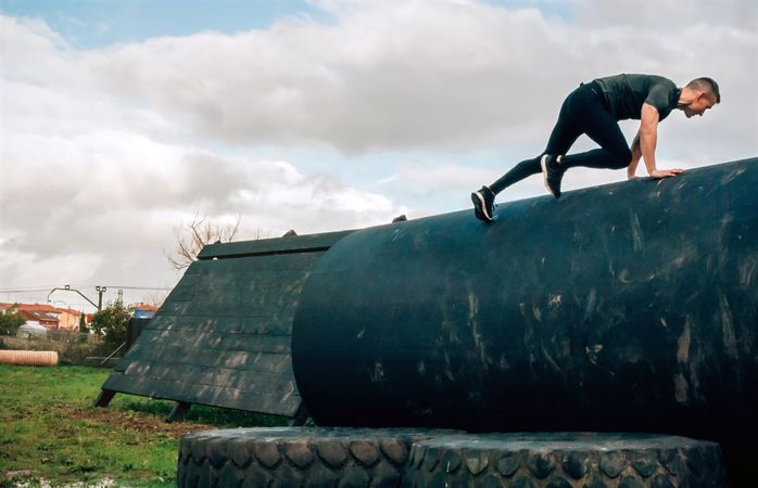Man in an obstacle course climbing a drum