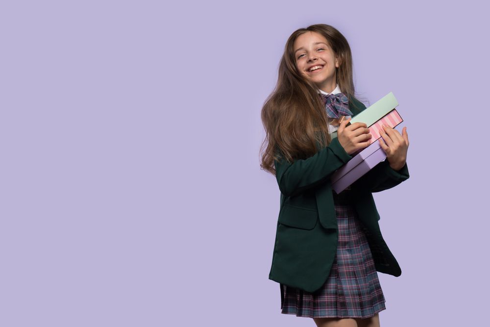 Smiling schoolgirl holding gift boxes in uniform.