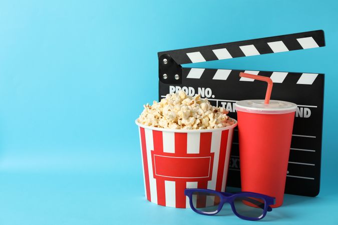 Clapperboard, bucket with popcorn, drink and 3d glasses on blue background