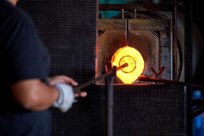 Glass blowers working on molten glass in factory