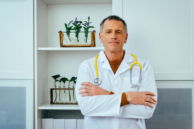Mature doctor standing in a clinical setting with arms crossed