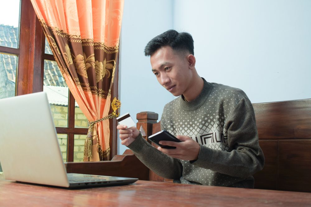 Serious Asian man in sweater shopping online holding credit card and smartphone