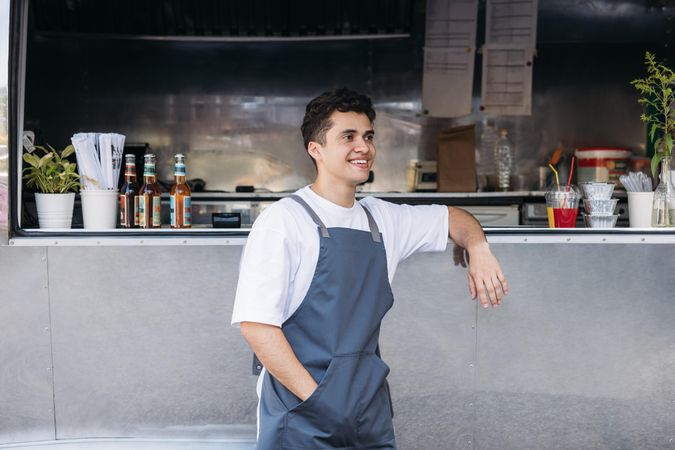 Smiling male in apron and leaning on open counter of food truck