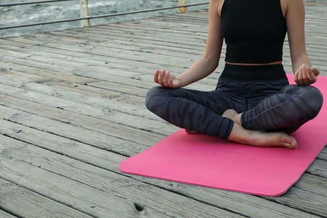 Young woman on yoga mat on wooden floor at sea, space for text