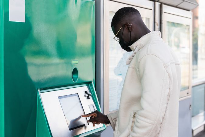 Black businessman touching screen of ATM in town
