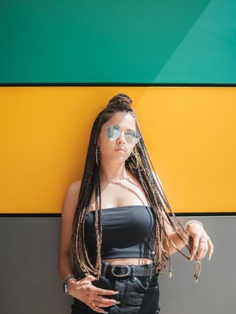 Charming teenage girl with dreadlocks in sunglasses nearby colorful wall