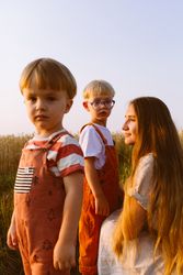 Adorable little kids standing near content young mom in agricultural field
