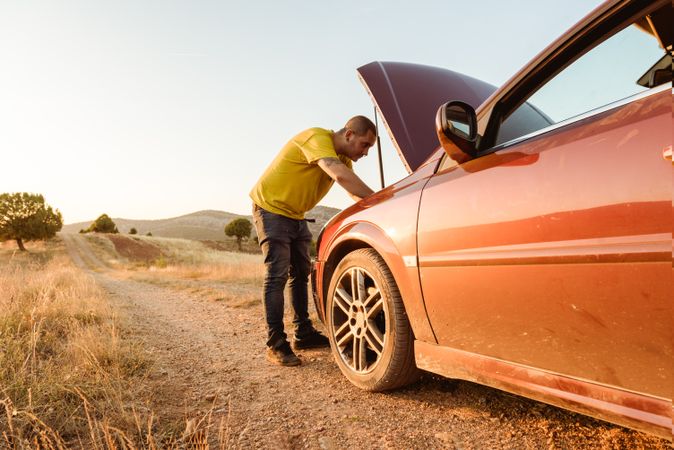 Man examining broken car in countryside